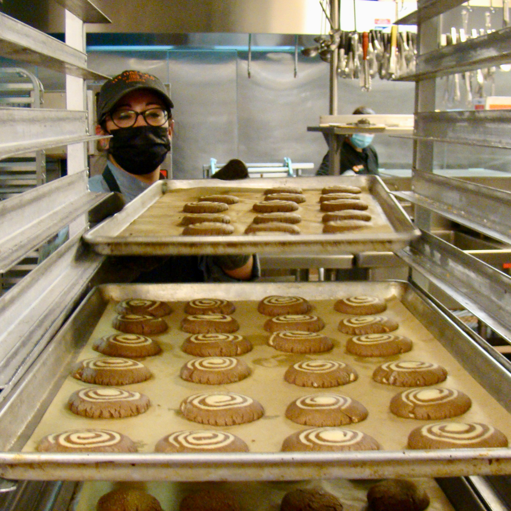 A chef slides a tray of cookies into a rack filled with more trays of cookies.