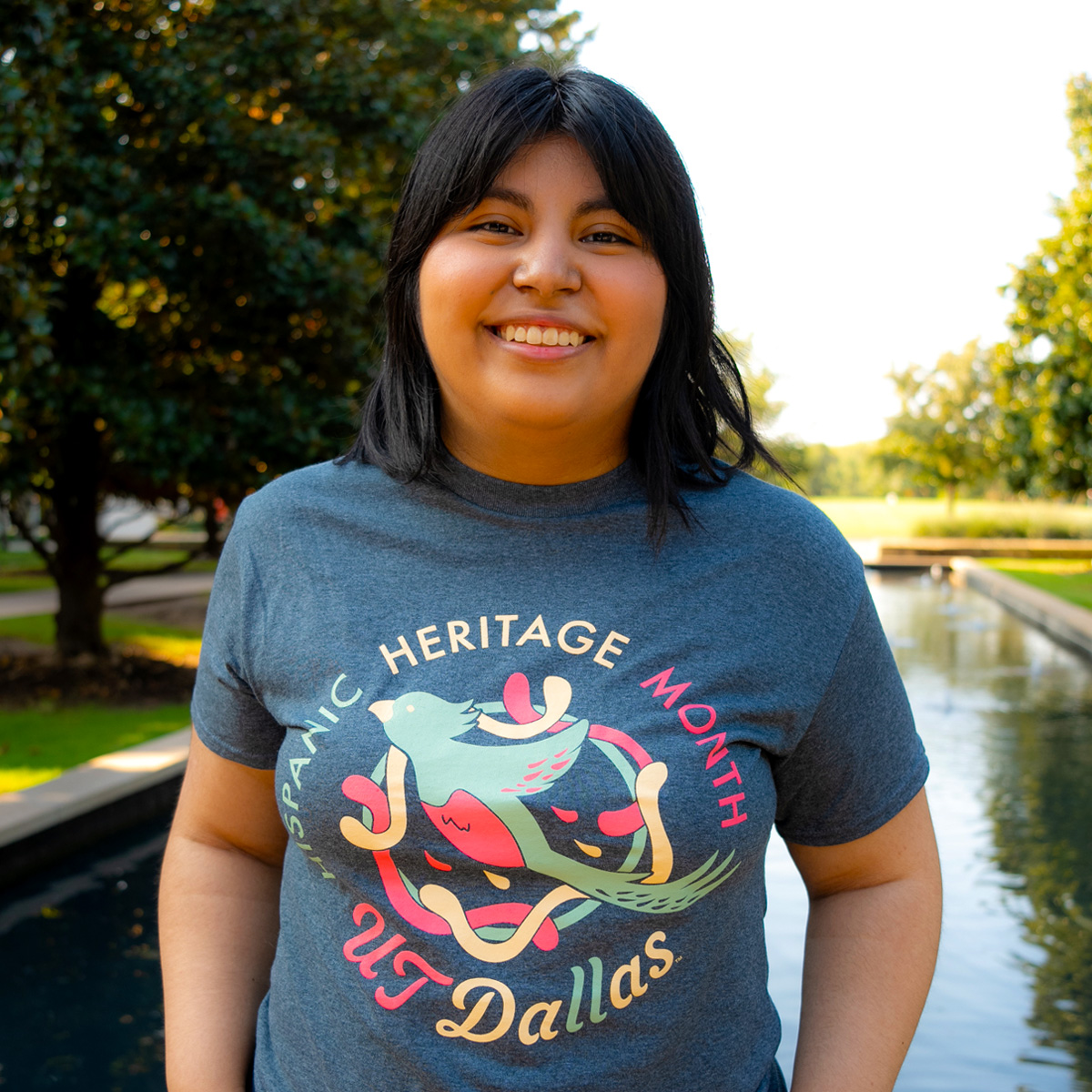 Vanessa Alvarez modeling her new Hispanic Heritage Month t-shirt in front of one of the reflecting pools on the UTD campus.