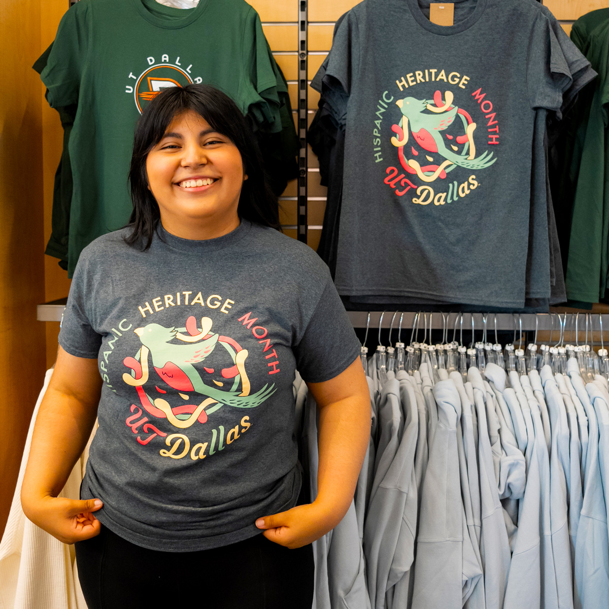 Vanessa Alvarez stands in a store in front of a rack of clothes where one of her t-shirts is on display.