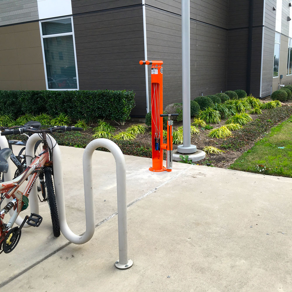 A UTD bicycle repair station next to a bike rack outside of University housing.