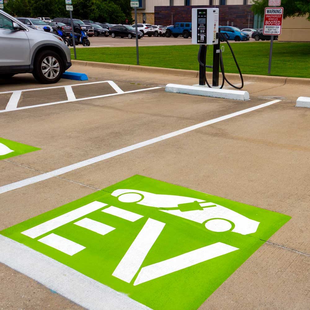 Parking spaces with electric vehicle chargers. the spaces are marked with a distinctive green and white symbol that includes the letters “EV”.